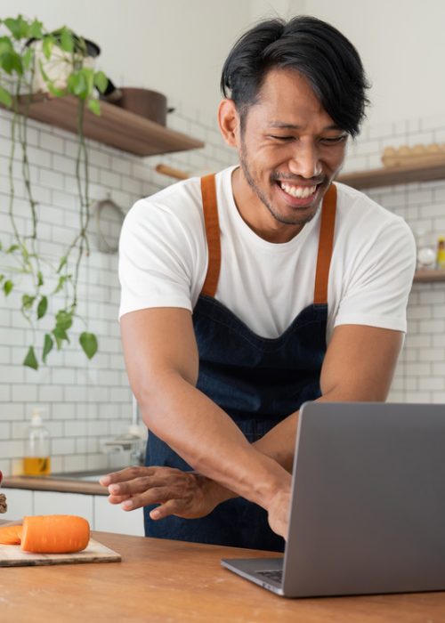 man-in-kitchen-looking-at-recipes-on-laptop-while-PCV6SLY.jpg